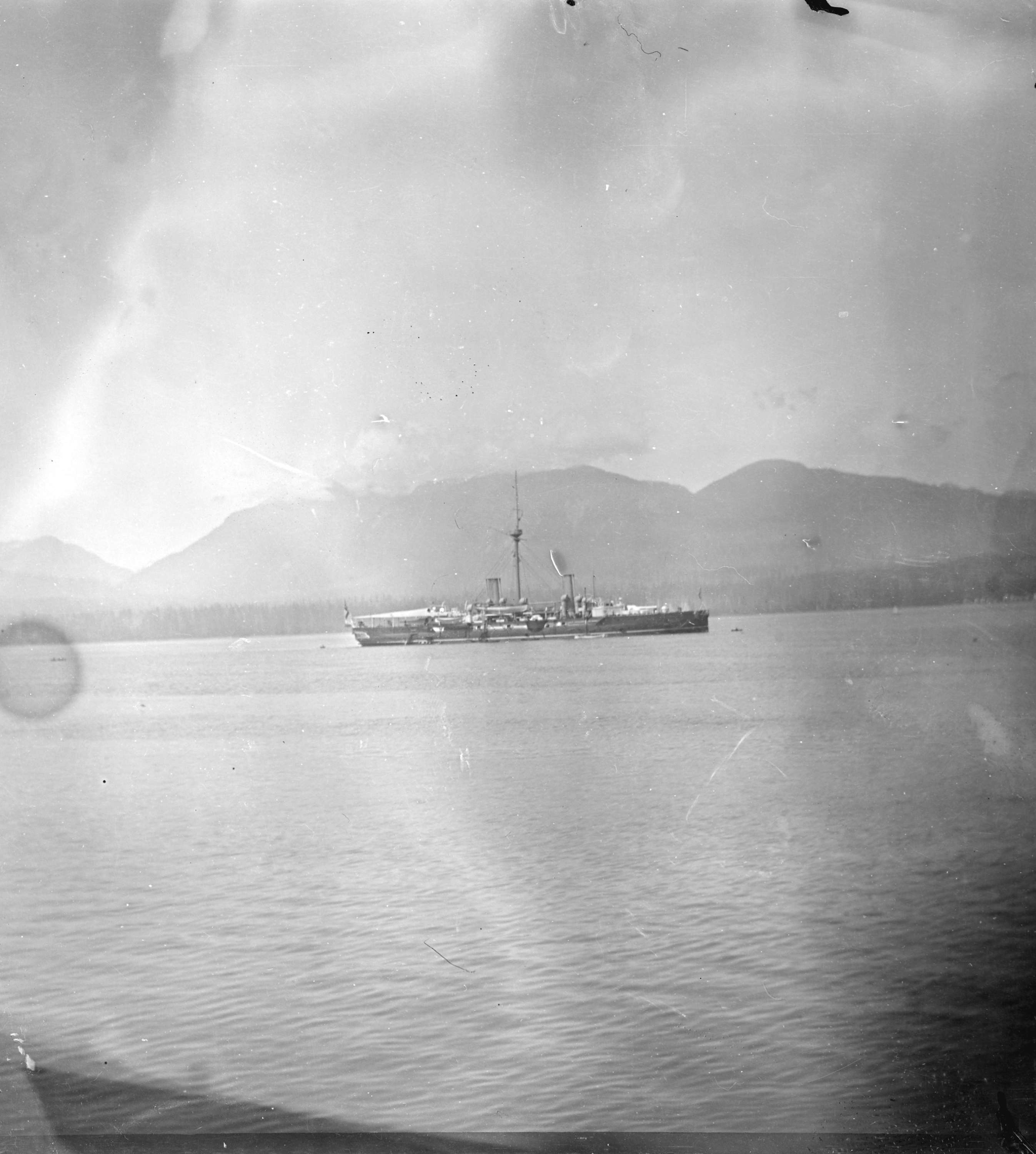 HMS Warspite at anchor in Vancouver Harbour, British Columbia, 1900, with smaller vessels and the waterfront visible
