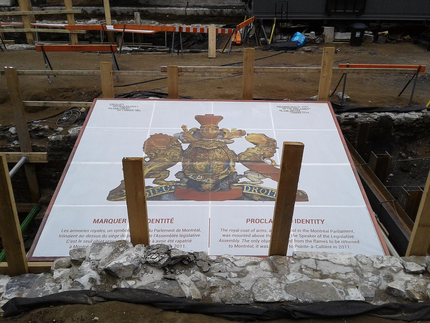 Archaeological excavation of the Sainte-Anne market and parliament site in Old Montreal, with an interpretive panel showing the royal coat of arms laid over the foundations