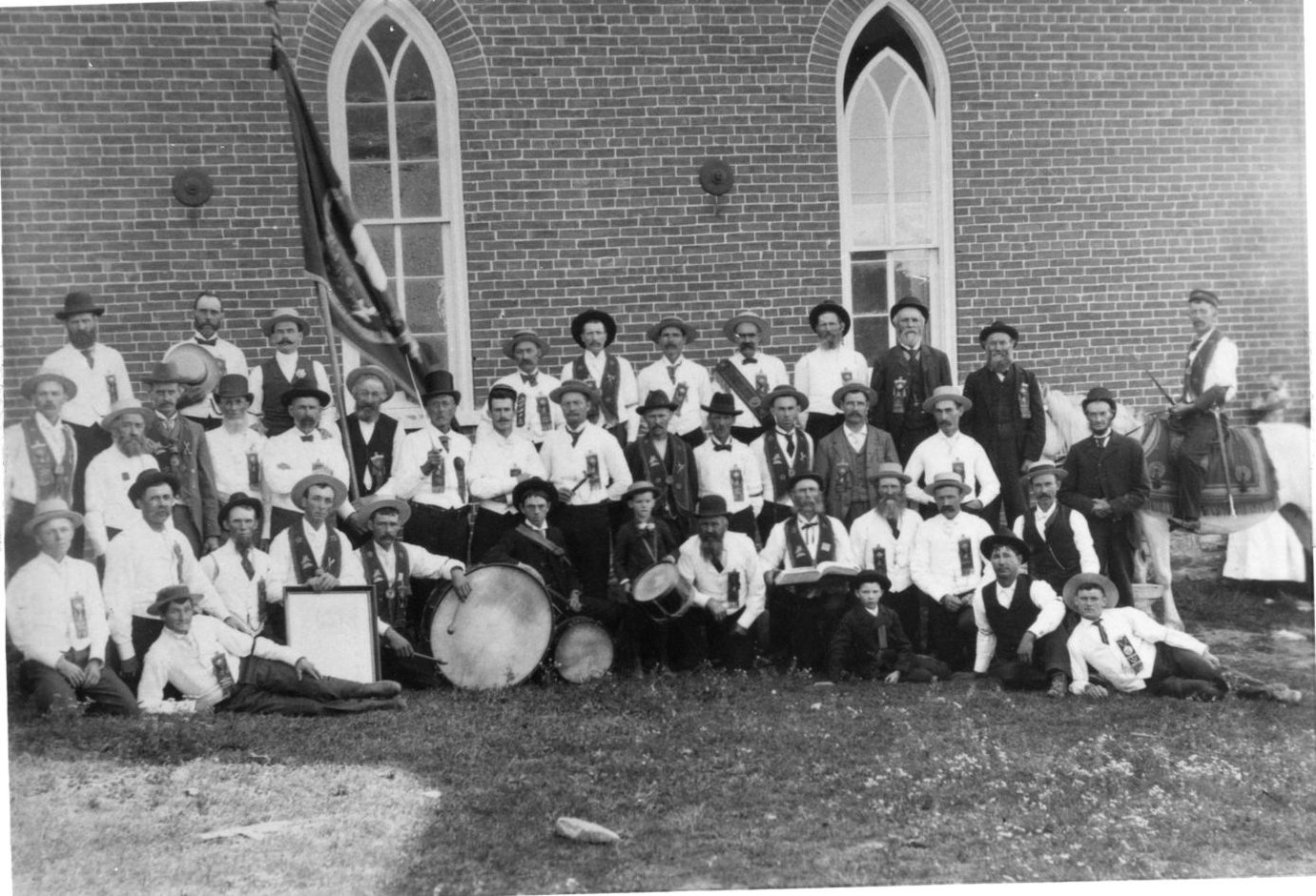 A large group of men and women in Orange regalia with a bass drum, assembled outside the Loyal Orange Lodge at Ivanhoe, Huntingdon Township, Hastings County