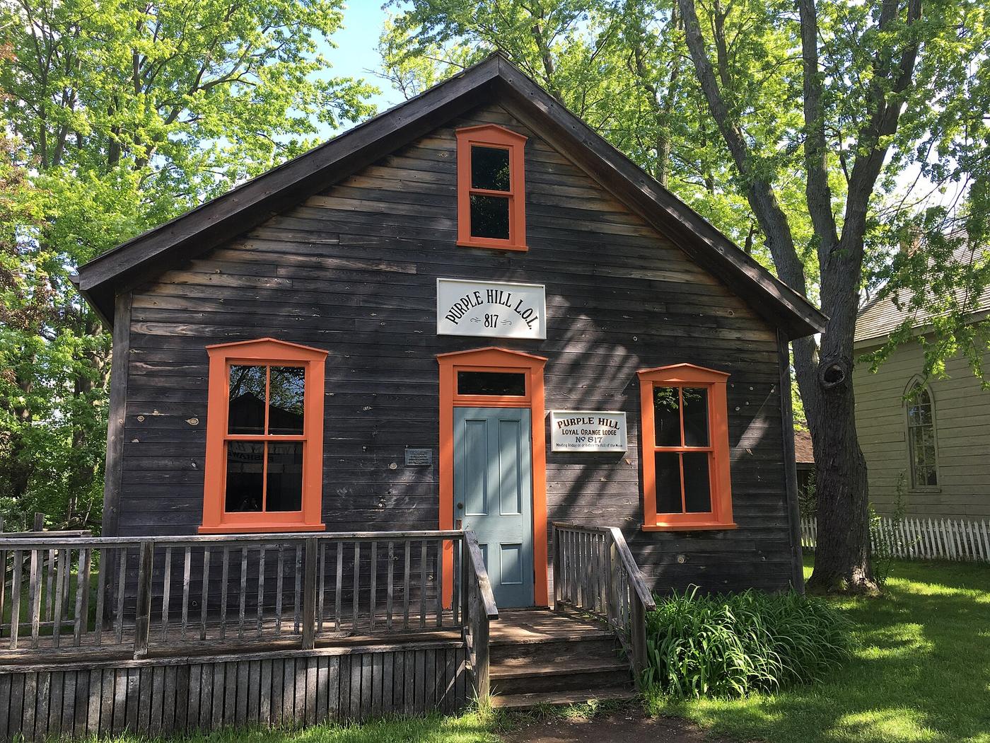 The relocated frame lodge building of Purple Hill Loyal Orange Lodge No. 817, with orange-painted window trim, at Fanshawe Pioneer Village near London, Ontario